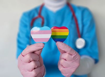 Healthcare worker holding heart-shaped LGBTQ+ and transgender flags.