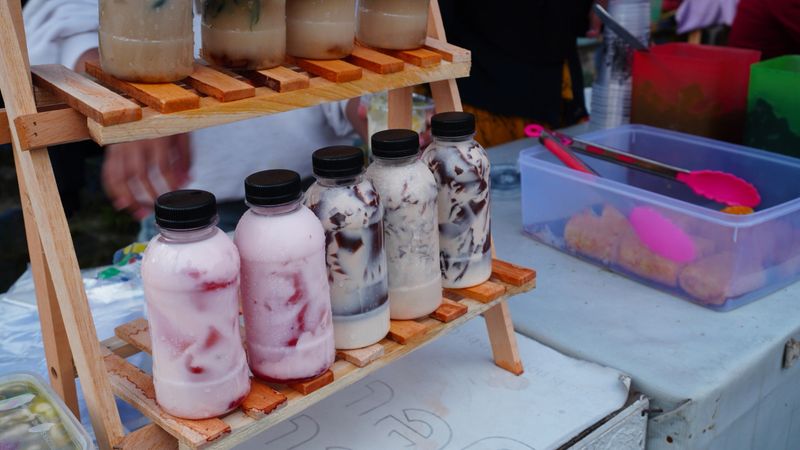 Fresh milk jelly drinks are organized on a wooden rack at a local stall the plastic bottles reveal the drink’s silky milk and wobbly jelly layers enticing passersby with their visual and flavorful charm