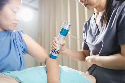 A healthcare professional uses a device on a patient's arm in a clinical setting.