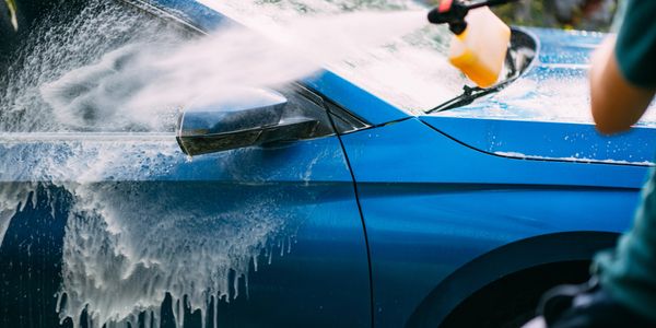 Person washing a blue car with soap and water.