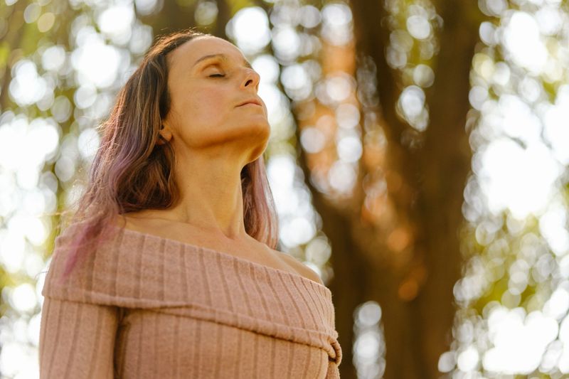 Serene woman enjoying the fresh air in a sunny forest, taking a deep breath and connecting with nature