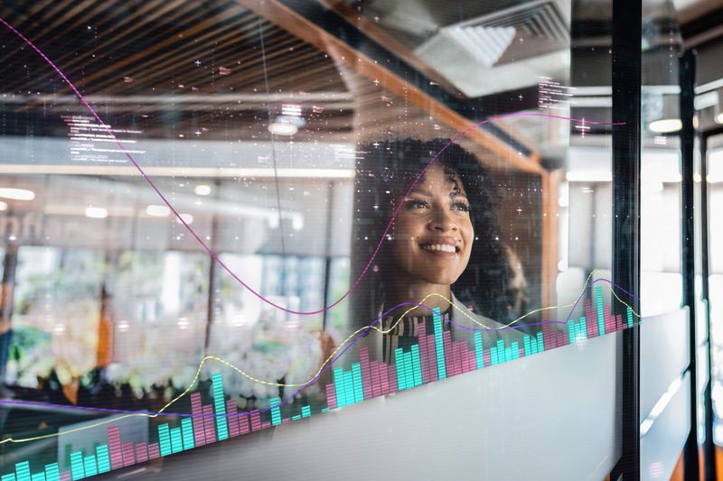 Businesswoman looking at data visualizations on glass wall in modern office
