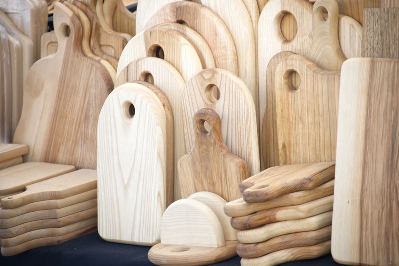 Close-up of handmade wooden cutting boards stacked in a variety of sizes and shapes, showcasing craftsmanship and natural wood grain.