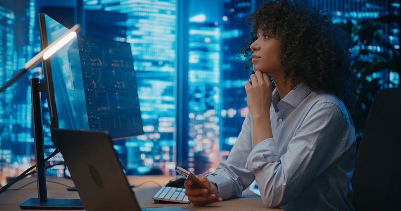 Financial advisors observe and analyze stock market charts, discussing prices, potential consequences, and developing investment strategies for the future. Modern office in skyscarper on high floor.