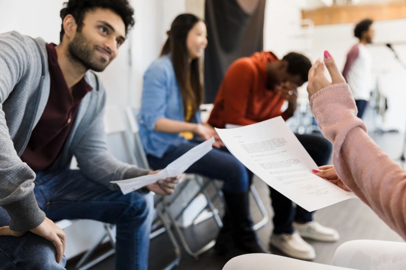 Diverse group of adults in casual wear participate in a therapy session, holding papers, engaged in discussion.