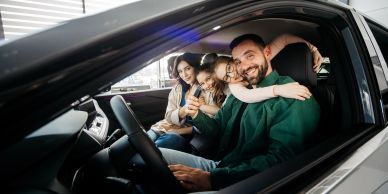 Happy family sitting in a new car with car keys, smiling.