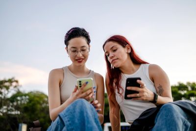 Two women outdoors looking at smartphones together.