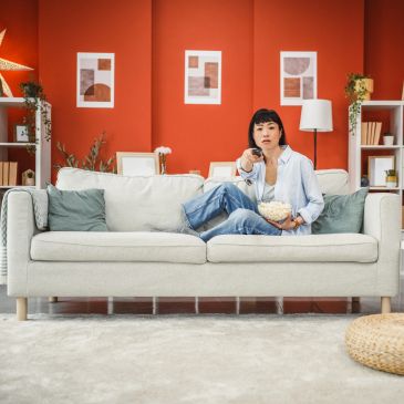 Jeune femme regarde la télévision en mangeant du pop-corn sur le canapé.