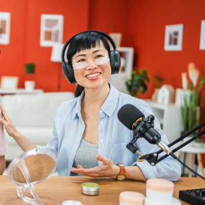 Woman podcasting with skincare patches and headphones in a cozy studio.