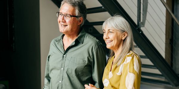 Smiling elderly couple standing together indoors near stairs.