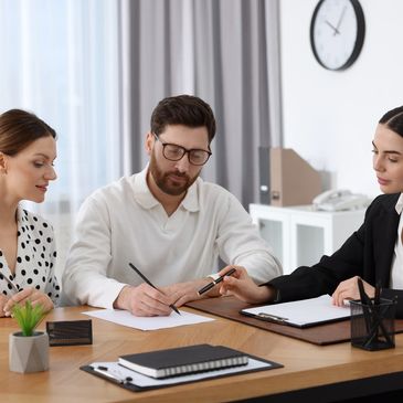 A man signs documents with two women assisting him in a modern office.