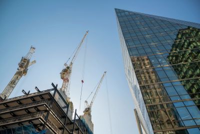 Cranes and modern glass building under blue sky.
