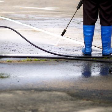 Person in blue boots pressure washing an outdoor surface.