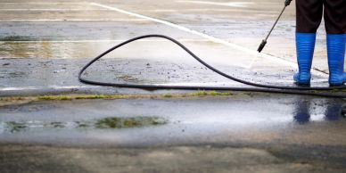 Person power washing an outdoor surface wearing blue boots.