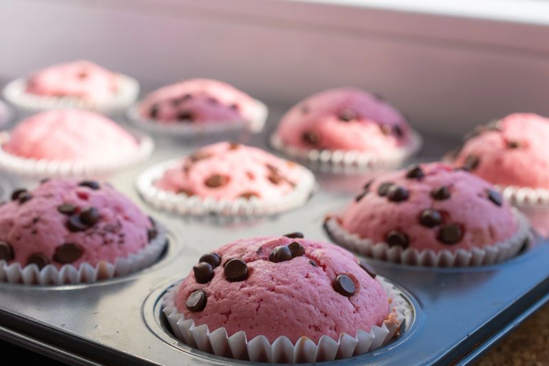 Tray of pink muffins with chocolate chips. The muffins are in paper cups and muffins pan.