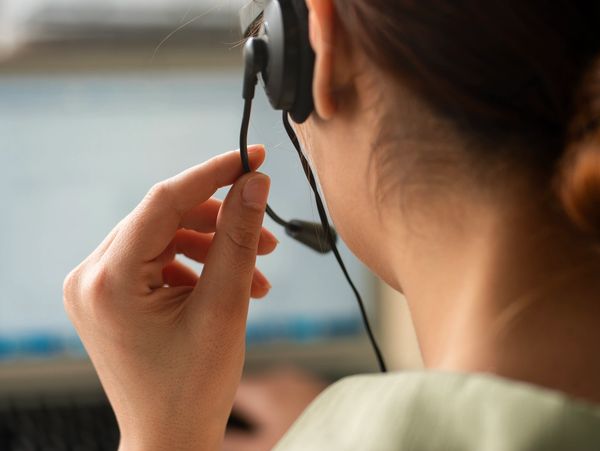 Person wearing a headset and adjusting the microphone while working on a computer.