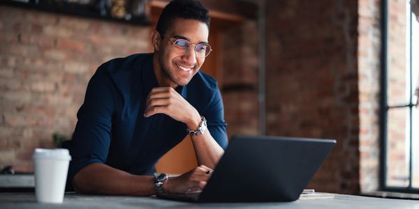 Smiling man working on a laptop in a cozy brick-walled room.