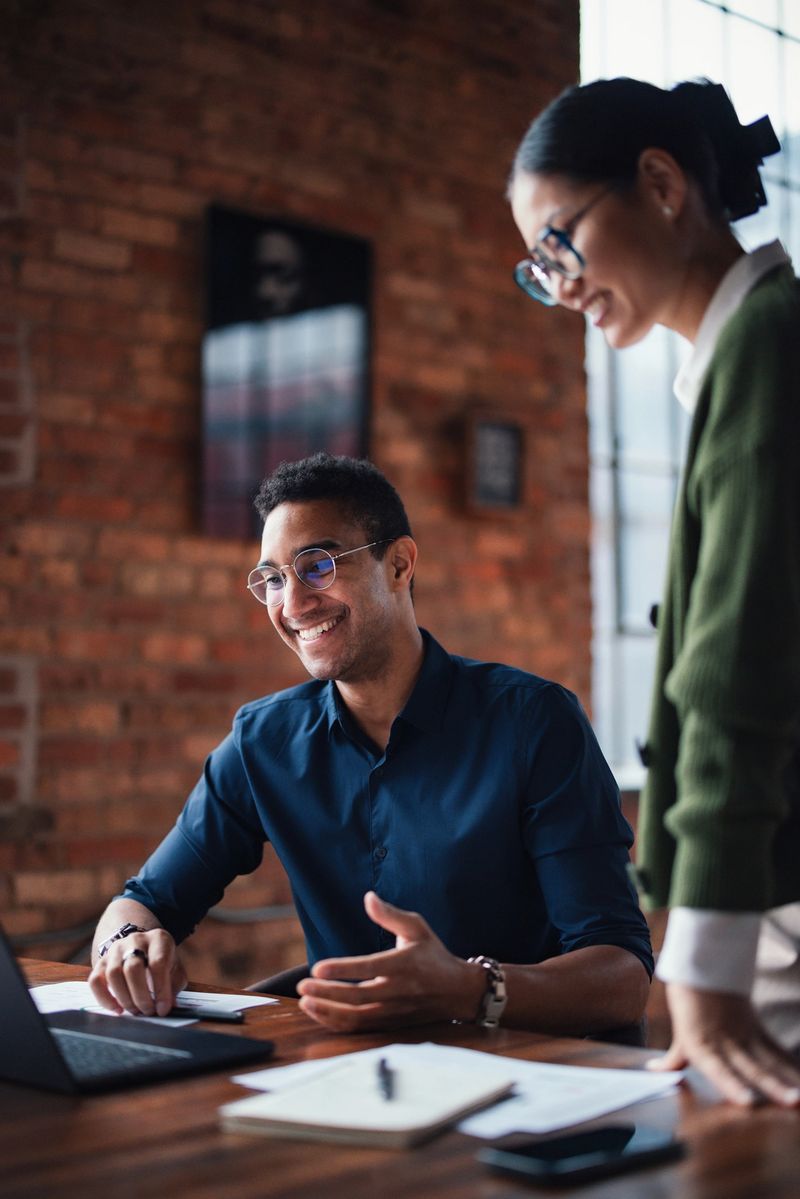 Office colleagues working together in a bright, modern setting with a focus on teamwork and professionalism. They appear engaged and productive, using technology and interacting with enthusiasm.