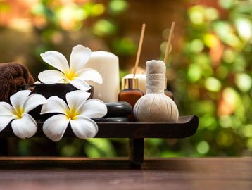 Spa essentials including flowers, candles, and massage tools on a wooden tray.