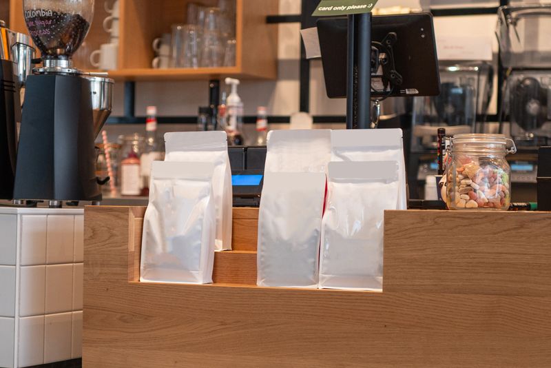 Blank white doypack packaging pouch bags on wooden shelf at coffee shop counter, ready for branding and sale