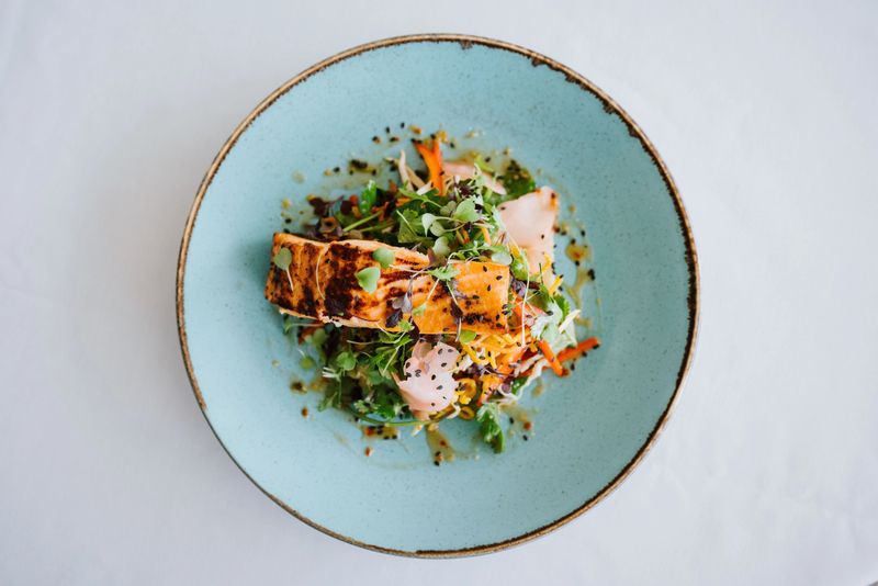 A gourmet dish of grilled salmon with fresh greens and vegetables served on a blue plate.