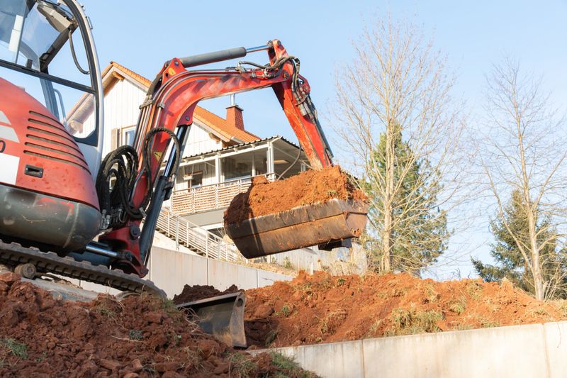 Mini-excavator in action during excavation works next to a residential house bucket filled with earth shot from below. High quality photo
