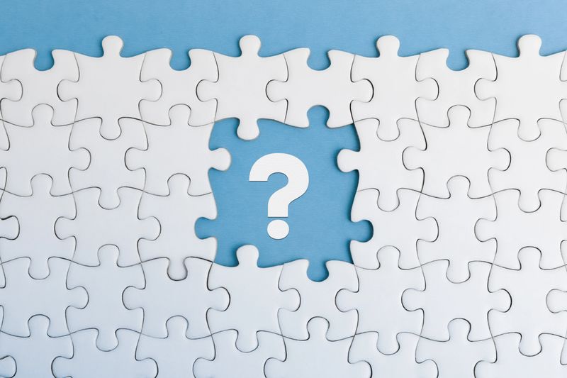 An incomplete jigsaw puzzle with a distinct absence of a white question mark piece on blue background, highlighting a sense of mystery or inquiry or a missing element in a solution.