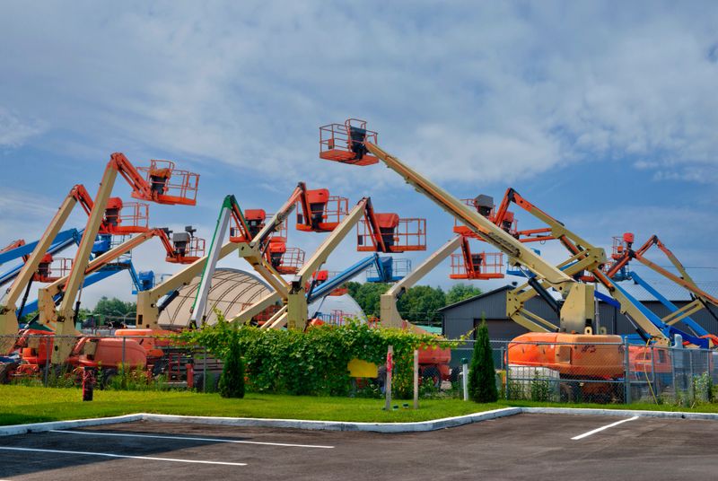 Outdoor lot filled with colorful boom lifts and aerial platforms lined up under a partly cloudy sky, showcasing heavy construction equipment ready for industrial or rental use.