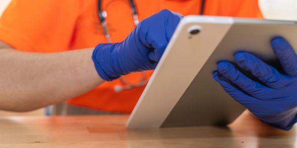 Healthcare worker wearing gloves using a tablet device.