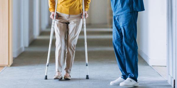 Person using crutches with nurse or doctor nearby.