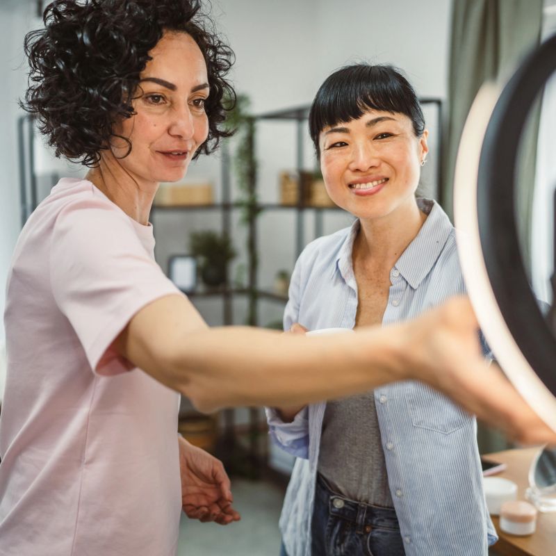 two mature multicultural woman prepare for record on mobile phone review and present skincare product for everyday use