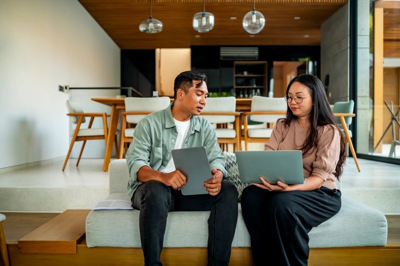 Two colleagues engage in a productive work discussion using laptops. The modern office setting emphasizes collaboration, teamwork, and a professional atmosphere conducive to creativity and innovation.