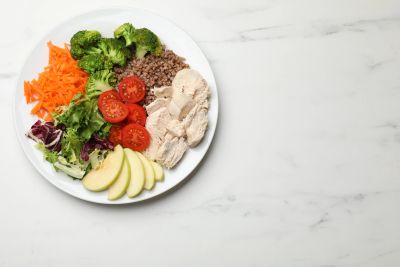 Healthy plate with chicken, vegetables, buckwheat, and apple slices.