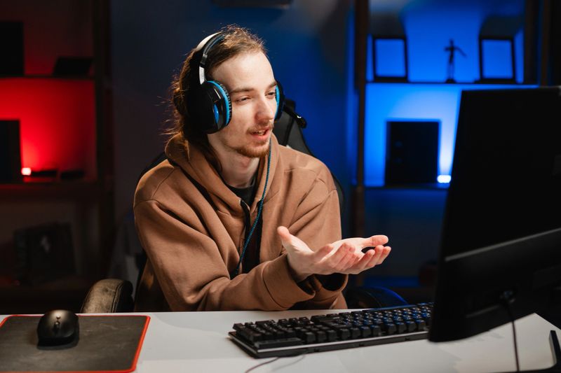 Male gamer in headphones asks for help shows palm up gesture in need play video game online in neon light at night. Gaming at Home. Online Multiplayer Championship. Esport streaming game. Copy space