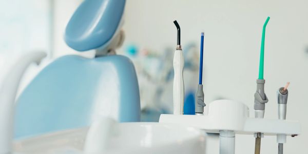 A blue dental patient chair next to dental suction tools, an air-water syringe and a dental curing l