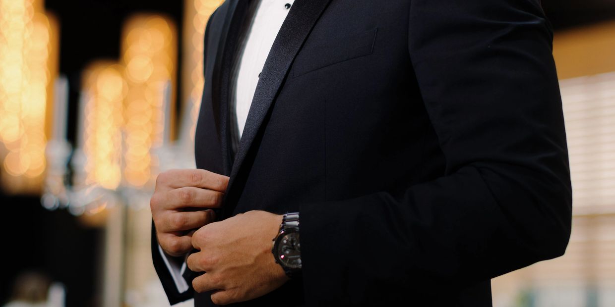 Man buttoning a black tuxedo jacket.