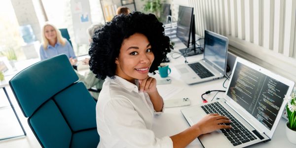 Smiling woman working on coding at her laptop in a modern office.