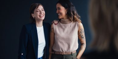 Dos mujeres sonriendo mientras una posa su mano en el hombro de la otra.