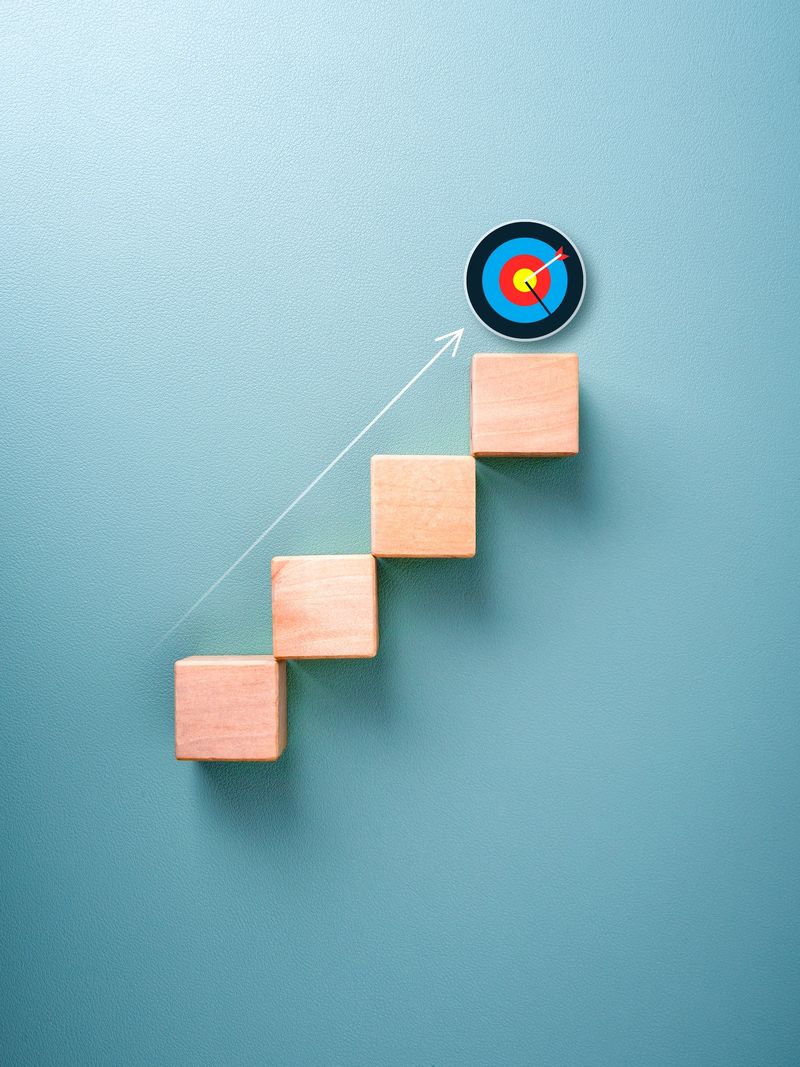 Target icon on top of wooden cube blocks with rising up arrows, 3d bar graph chart steps on vertical blue background. Business growth progress, profit, investment plan, economic improvement concepts.