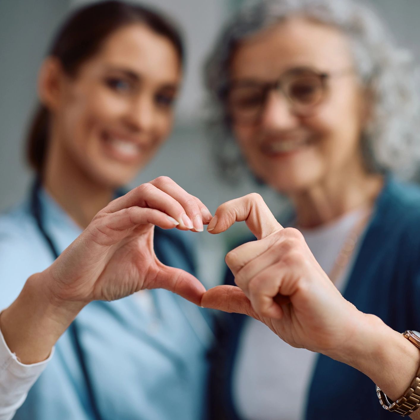 A nurse and elderly woman forming a heart shape with their hands.