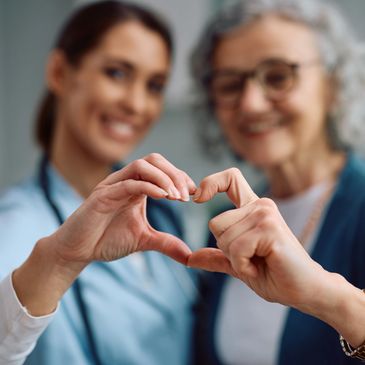 A nurse and elderly woman forming a heart shape with their hands.