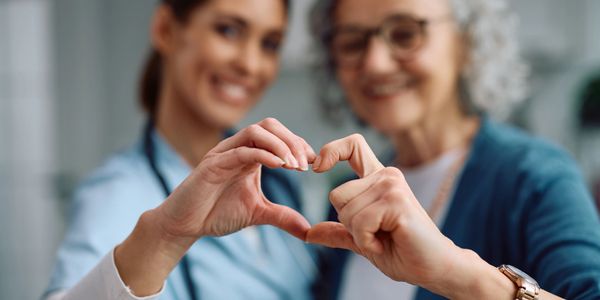 A nurse and elderly woman forming a heart shape with their hands.