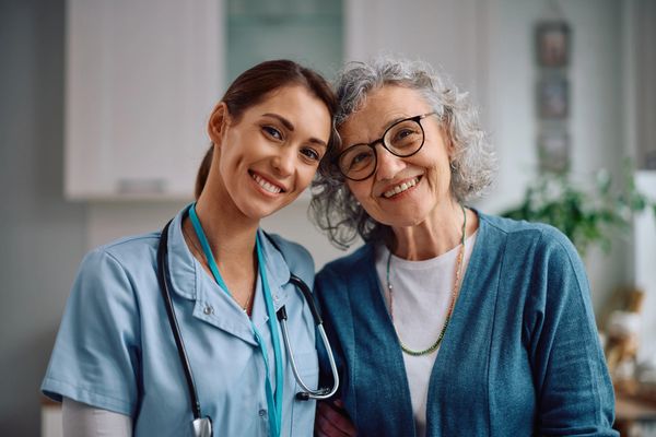 Smiling nurse and elderly woman pose together, showing warmth and care.
