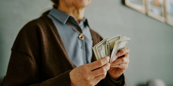 Elderly person counting US dollar bills indoors.