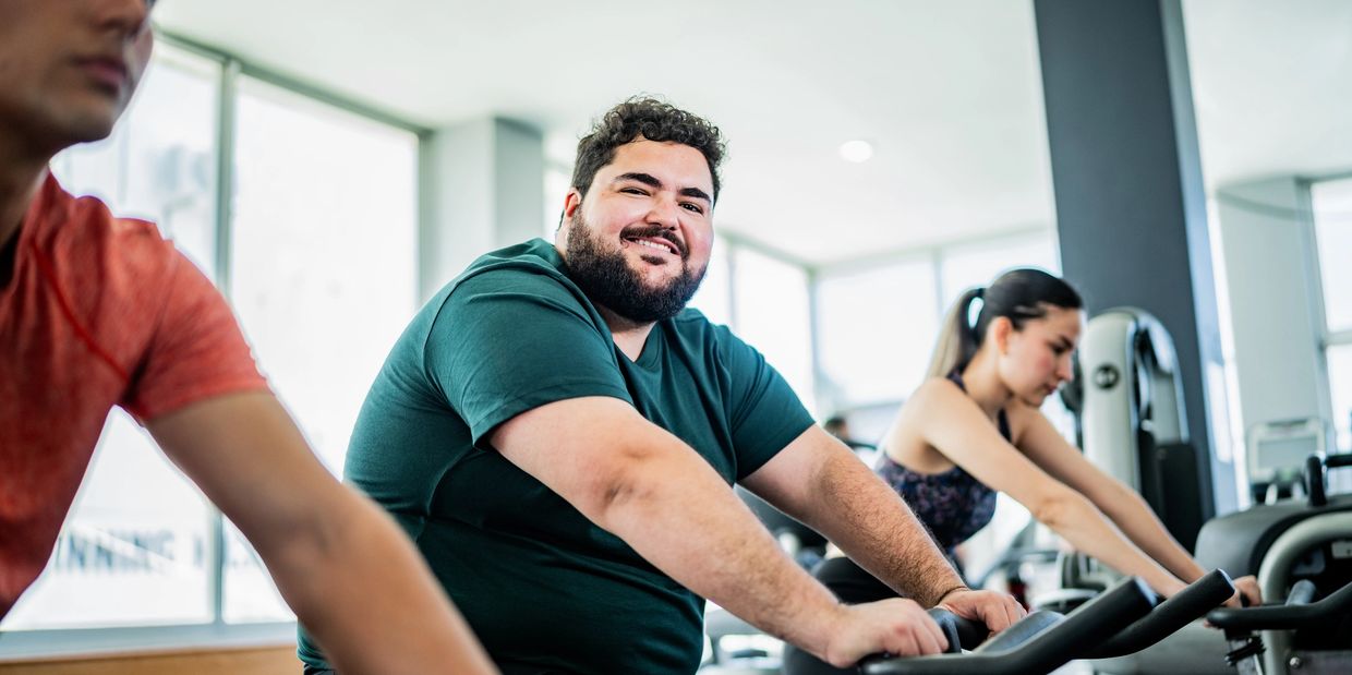 Smiling man working out on an exercise bike in a gym with others.
