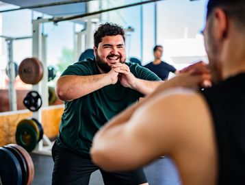 Two men exercising together in a gym, smiling and squatting.
