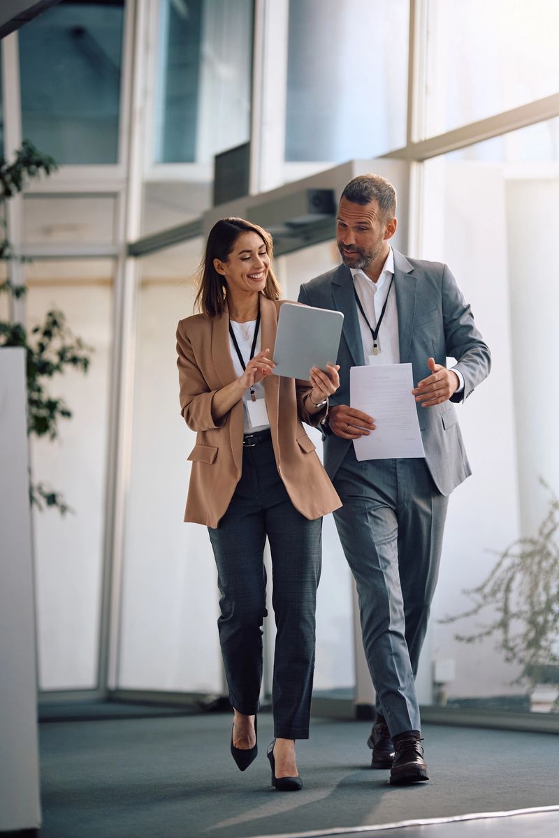 Smiling businesswoman and her coworker using digital tablet while walking through the office.