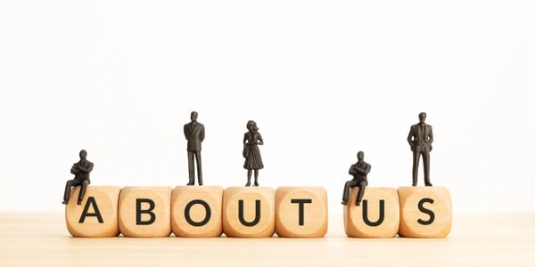 Miniature figures on wooden blocks spelling 'ABOUT US'.