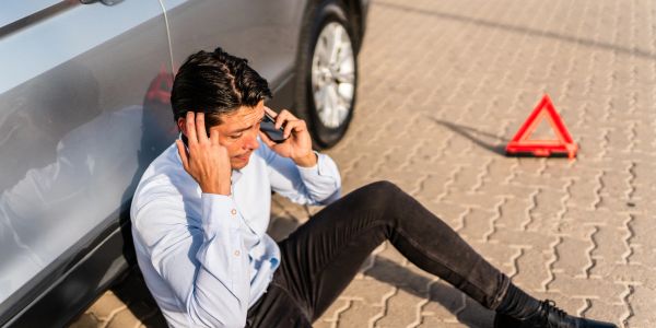 Man sitting on ground by car making a phone call after a car issue.