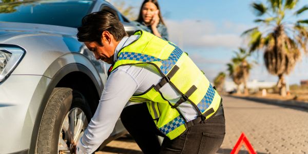 A man changes a car tire on the roadside.